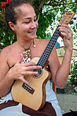 Schöne einheimische Frau spielt Ukulele neben dem Bora Bora Vaitape Dock, Gesellschaftsinseln, Französisch-Polynesien, Südpazifik.