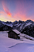 Einsame Berghütte im Tiefschnee mit majestätischen Gipfeln im Hintergrund in der Morgendämmerung, Tombal, Val Bregaglia, Graubünden, Schweiz, Europa