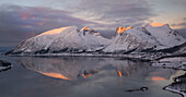 Dämmerungslicht über dem Dorf Bergsbotn und dem Bergsfjord mit dem Bergsbotn-Gebirge im Hintergrund im Winter, Senja, Troms og Finnmark, Norwegen, Skandinavien, Europa
