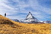 Wanderer steht vor der ikonischen Form des Matterhorns zwischen gelben Gräsern, Riffelalp, Zermatt, Kanton Wallis, Schweizer Alpen, Schweiz, Europa