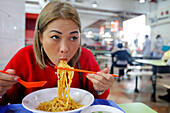 Junge Frau isst an einem traditionellen asiatischen Essensstand im Singapore Food Trail hawker center, Singapur, Südostasien, Asien