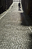 An Old Man Walking Along A Cobbled Street.