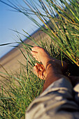 Beine einer Person auf Gras in den Sanddünen