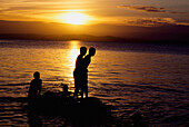 Silhouetten von Jungen auf Felsen am Lake Taupo bei Sonnenuntergang