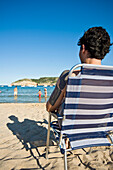 Mann entspannt im Liegestuhl am Strand von Cala Mongo
