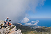 Zwei Wanderer sitzen auf dem Gipfel des Texi-Gebirges und blicken auf die Aussicht, Seitenansicht