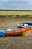 Boats In Mud Of Small Estuary By Marshes
