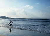 Mann mit Surfbrett läuft am Strand