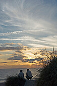 Zwei Menschen beobachten den Sonnenuntergang am Strand, Ohrenblick, Jütland, Dänemark