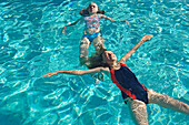 Two Girls (12-13) Floating On Water In Swimming Pool