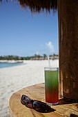 Cocktailgetränk und Sonnenbrille auf Strandtisch an der Riviera Maya, Yucatan-Halbinsel, Staat Quintana Roo, Mexiko