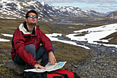 Wanderer, der auf dem Boden sitzend die Karte prüft, Kungsledden Trail, Schweden