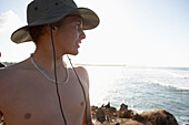 Junger Mann mit Hut schaut vom Ufer auf das Meer, britischer Surfer Josh Hughes in Tansania, Ostafrika