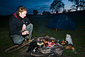 Mann kocht über der Holzkohlenglut eines Holzfeuers, Dartmoor National Park,Postbridge,Yelverton,Devon,Uk