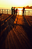 Familie betrachtet den Sonnenuntergang über der Stadt und dem Meer vom Brighton Pier aus, Brighton, England