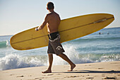 Mann trägt Surfbrett am Strand von Bondi