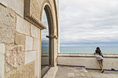Eine junge Frau blickt über eine Mauer auf das Meer im Maricel-Palast; Sitges, Provinz Barcelona, Spanien.