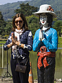 Eine Touristin posiert in einer ähnlichen Pose wie eine thailändische Statue, neben der sie steht; Tambon Pa Tueng, Chang Wat Chiang Rai, Thailand.