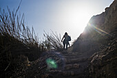 Eine junge Frau wandert die zerklüfteten Steintreppen in Ein Gedi hinauf, während das Sonnenlicht den Himmel erhellt; Süddistrikt, Israel.