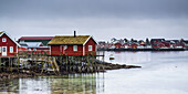 Red Buildings Along The Water's Edge Under A Cloudy Sky; Lofoten Islands, Nordland, Norway