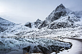 Schneelandschaft mit zerklüfteten Bergen, die sich in ruhigem Wasser spiegeln; Lofoten, Nordland, Norwegen