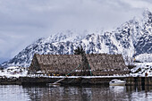 Ein spitz zulaufendes Gebäude am Rande des Wassers, das Schutz für die Ausrüstung bietet, mit einem im Wasser vertäuten Boot; Svolvar, Lofoten, Nordland, Norwegen