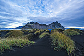 Person stehend auf einem schwarzen Sandhügel mit Blick auf Vestrahorn oder Stokknes an der Südküste Islands; Hofn, Island