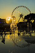 Springbrunnen und ein Riesenrad bei Sonnenuntergang, das sich im Wasser spiegelt, Place Massena; Nizza, Cote D'azur, Frankreich