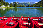 Red boats lined up at Champex Lake under blue sky with a mountain range in the background; Champex, Valais, Switzerland