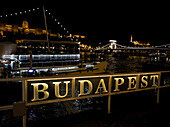 Szechenyi Chain Bridge over the Danube River and sign for Budapest illuminated at nighttime; Budapest, Budapest, Hungary