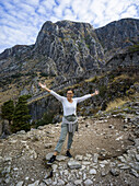 A woman stands posing in front of the stone walls and rugged mountains at Kotor Fortress; Kotor, Montenegro