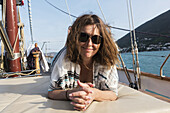 A woman lays on a the deck of a sailboat with windswept hair looking at the camera on the coast of Montenegro; Montenegro