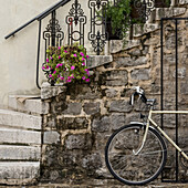 Ein an einer Steinmauer geparktes Fahrrad mit Stufen, die nach oben führen, und Pflanzen, die das Geländer schmücken; Budva, Opstina Budva, Montenegro