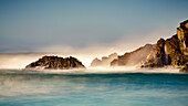 Mist over the turquoise water along the rugged coastline; Big Sur, California, United States of America