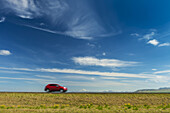 Red car driving on open road near Hella with Hekla volcano in the distance; Iceland