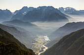 Sunrise with illuminated fog laying through the mountain range and over a valley; Sesto, Bolzano,Italy