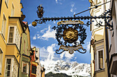 Nahaufnahme eines dekorativen Metallschildes mit schneebedeckten Bergen und blauem Himmel im Hintergrund; Innsbruck, Tirol, Österreich