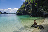 Eine Frau im Bikini sitzt auf einem Felsen entlang einer tropischen Küste; Andamanen, Indien.