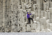 Eine Touristin posiert auf den Basaltfelsen am Strand von Reynisfjara in Südisland; Island