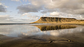 Feuchter schwarzer Sandstrand an der Küste Islands mit Klippen, die sich im Wasser spiegeln; Grundarfjorour, Island