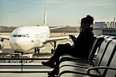 Passenger sitting in airport terminal using her smart phone, Beijing Capital International Airport; Beijing, China