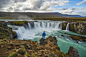 Mann steht oberhalb des Wasserfalls Godafoss, Nordisland; Island