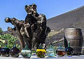 Alter Baumstumpf, Weinflaschen und Weinfass vor einer Bodega; Lanzarote, Spanien