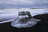 Large chunk of ice sitting on the shore of Iceland with dramatic skies in behind it, near Jokulsarlon ice lagoon; Iceland