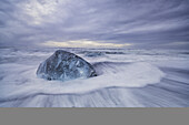 Large ice block laying on the shores of Southern Iceland while waves crash on shore; Iceland