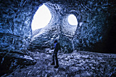 Person standing underneath the openings of a glacier, South Iceland; Iceland