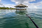 Ein Boot paddelt über türkisfarbenes Wasser mit einem Unterstand am Ende des Docks und der Küstenlinie einer Karibikinsel; Honduras