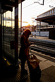 Eine Frau steht mit ihrem Koffer auf dem Bahnsteig eines Bahnhofs neben den Gleisen und benutzt ihr Smartphone; St. Gallen, St. Gallen, Schweiz