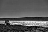 Schwarz-Weiß-Bild eines Paares, das am Dillon Beach am Wasser sitzt und auf den Ozean hinausschaut; Kalifornien, Vereinigte Staaten von Amerika.