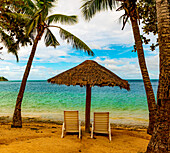 Zwei Stühle unter einem strohgedeckten Sonnenschirm am Strand mit Blick auf das türkisfarbene Wasser des Ozeans; Malolo Island, Fidschi